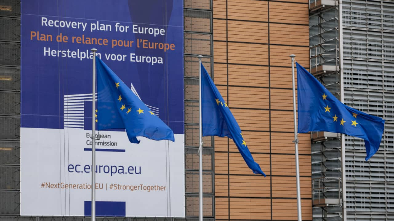 Palazzo del Parlamento UE con bandiera europee e un cartellone che parla del next generation eu.