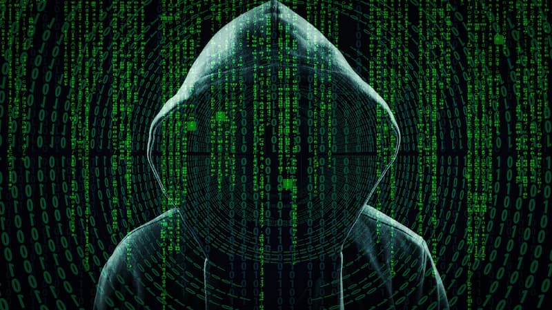 Sagoma di hacker con cappuccio dietro uno schermo con codice, simbolo cyber security nel rapporto Clusit 2022 edizione ottobre