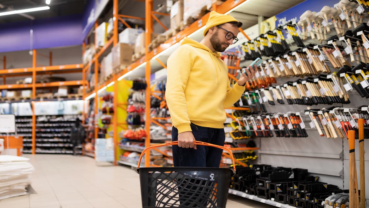 Uomo con smartphone accanto a uno scaffale fa webrooming per il black friday